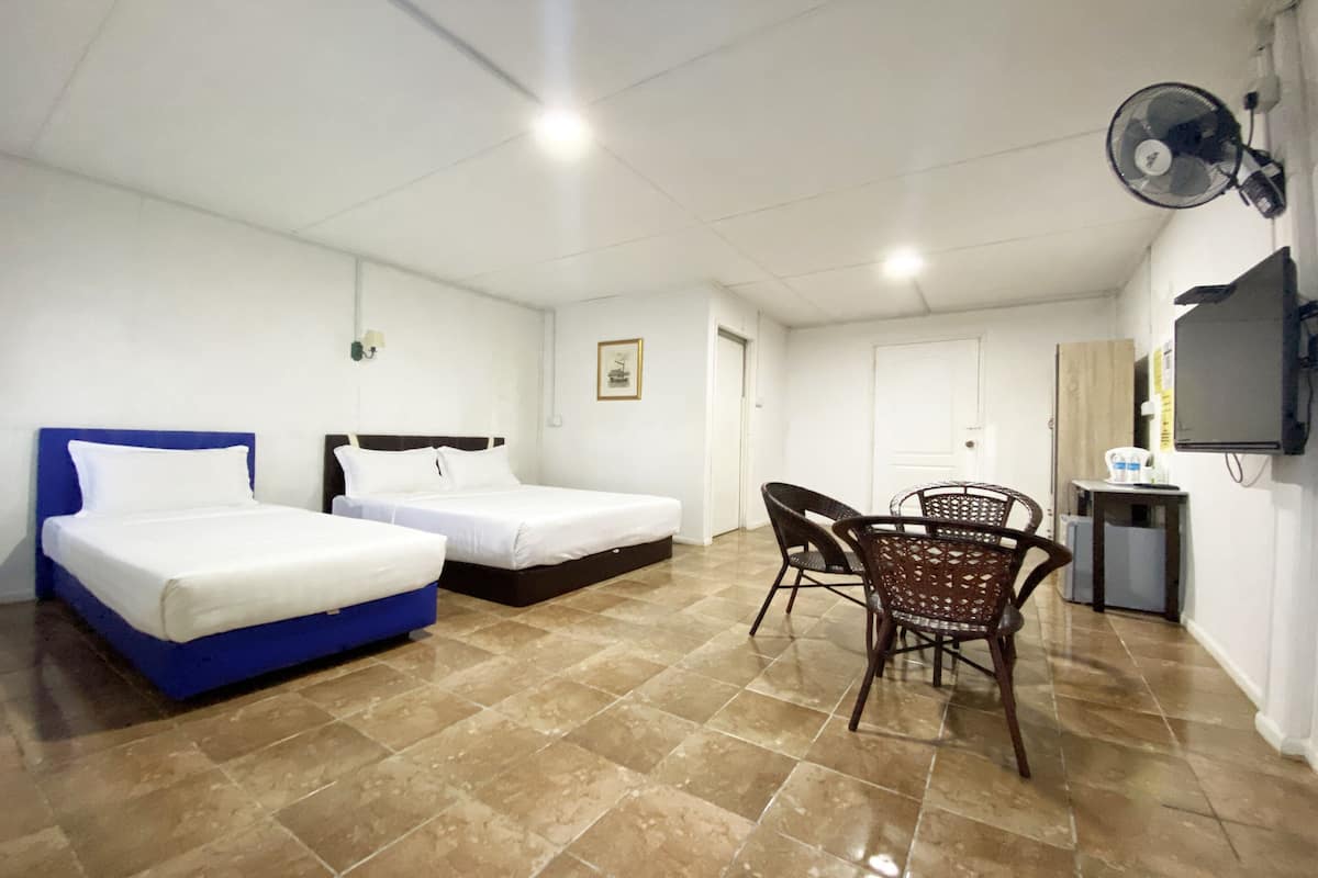 A hotel room with two beds, a dining area with chairs, a fan, a TV, and a small table with items on it.