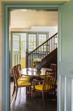 Un coin repas avec une table et des chaises en bois, un vase rempli de fleurs et un escalier en arrière-plan.