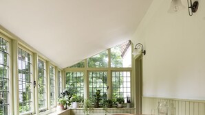 Una habitación iluminada por el sol, con piso de madera, una mesa redonda con sillas y una ventana con vista a follaje.