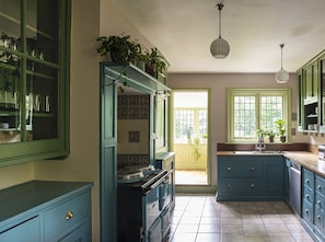 A kitchen with teal cabinets, a stove, and a sink. There are potted plants on the windowsill and a hanging light fixture.