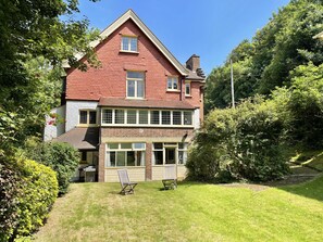 Une maison à deux étages, avec un toit rouge, de grandes fenêtres et une pelouse bien entretenue.