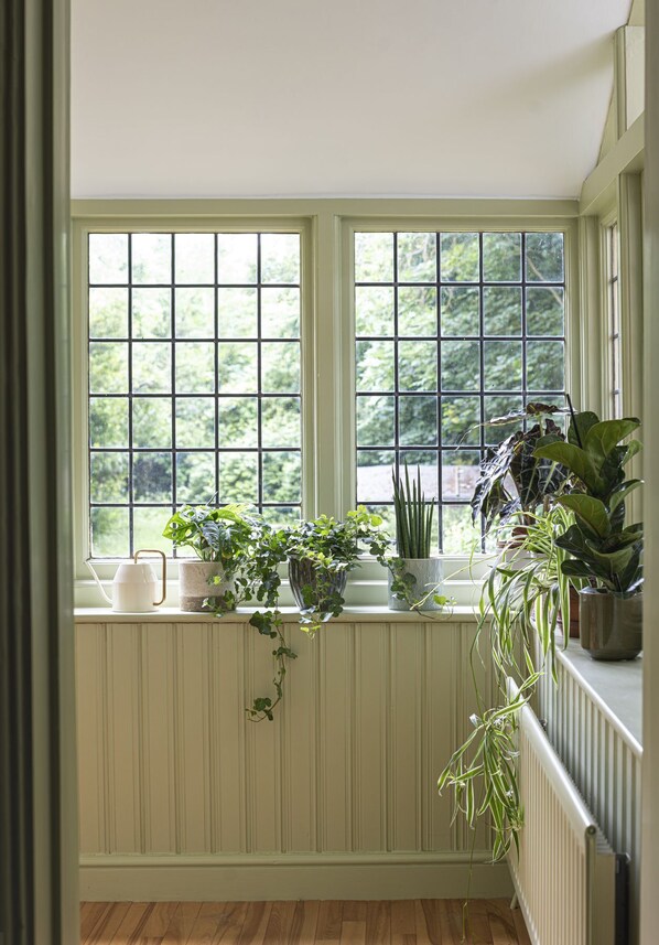 Una habitación con ventanal que da a un jardín, con diversas macetas y un radiador blanco.