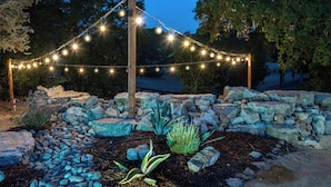 A garden with a stone wall, a wooden post, and string lights. - Spa + Fire Pit + Court | Paso Robles Wine Country | Na Hoku Ranch (Atascadero)