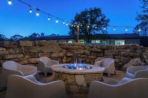 An outdoor seating area with stone walls and a fire pit, surrounded by chairs and string lights.