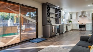 A spacious kitchen with modern appliances, a dining area with a sofa, and a sliding glass door leading to an outdoor patio. - Spa + Fire Pit + Court | Paso Robles Wine Country | Na Hoku Ranch (Atascadero)