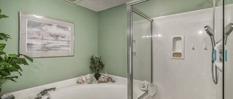 A bathroom with a bathtub, a glass-enclosed shower, a sink, and a framed picture on the wall.