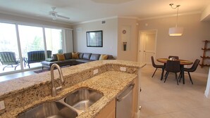 A modern kitchen with granite countertops, stainless steel appliances, and a dining area with a round table and chairs. - Updated Modern Poolside Condo! (Bonita Springs)