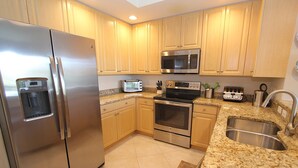 A modern kitchen with stainless steel appliances, wooden cabinets, granite countertops, and a built-in oven. - Updated Modern Poolside Condo! (Bonita Springs)
