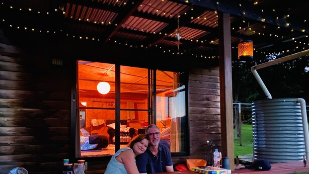 A wooden deck with a table, a metal water tank, and string lights. - Unique funky Arthouse ‘Franks Place’ Hunchy Valley (Hunchy)