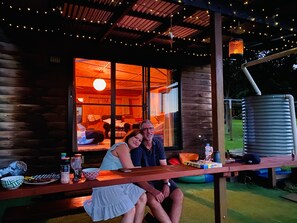 A wooden deck with a table, a metal water tank, and string lights. - Unique funky Arthouse ‘Franks Place’ Hunchy Valley (Hunchy)