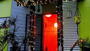 A house with a red-lit entrance, a covered porch with string lights, and potted plants. - Unique funky Arthouse ‘Franks Place’ Hunchy Valley (Hunchy)