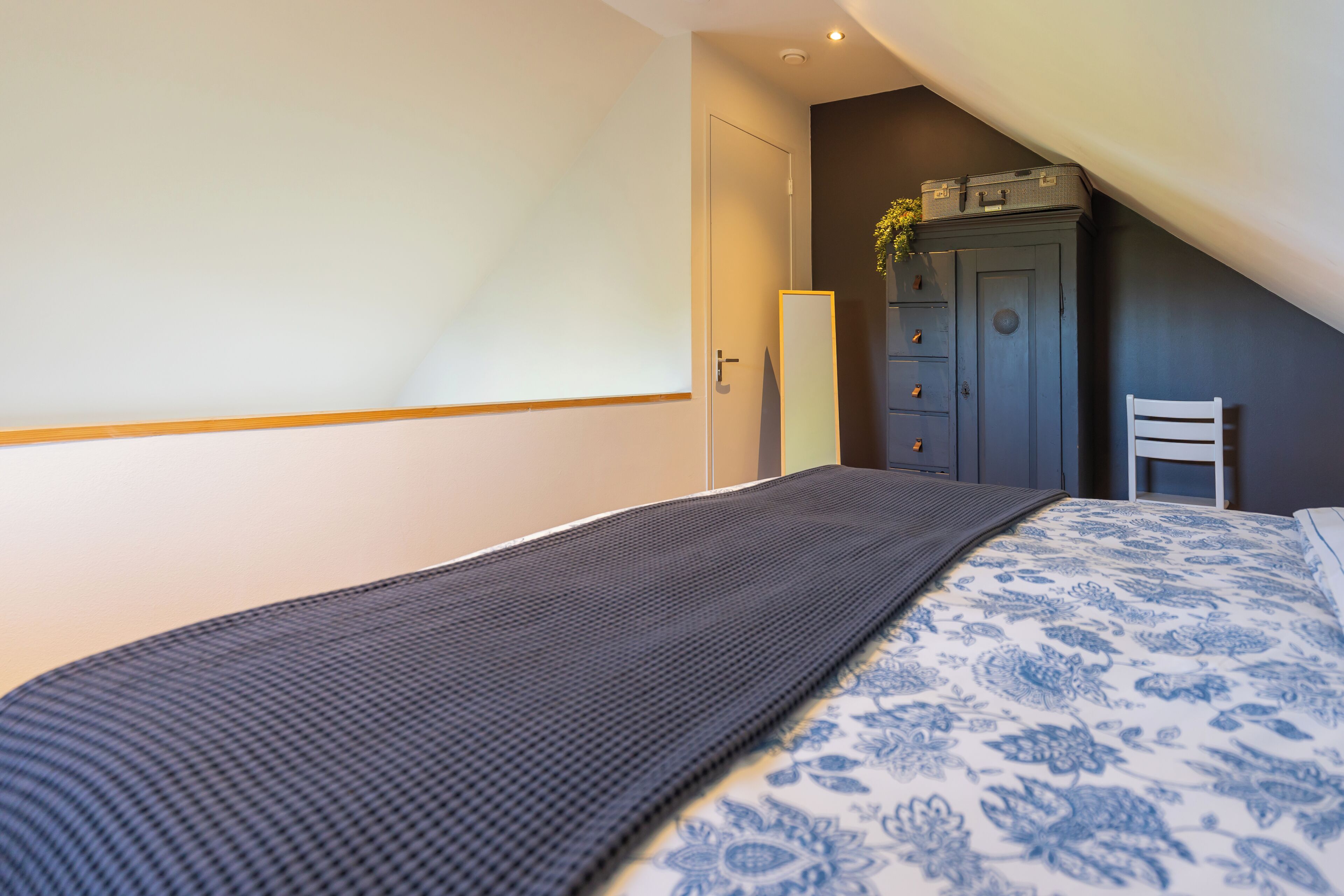 Een slaapkamer met een bed, een kledingkast, een stoel en een deur.