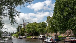 Un canal bordé de bateaux, un moulin à vent et des bâtiments le long de la rive.