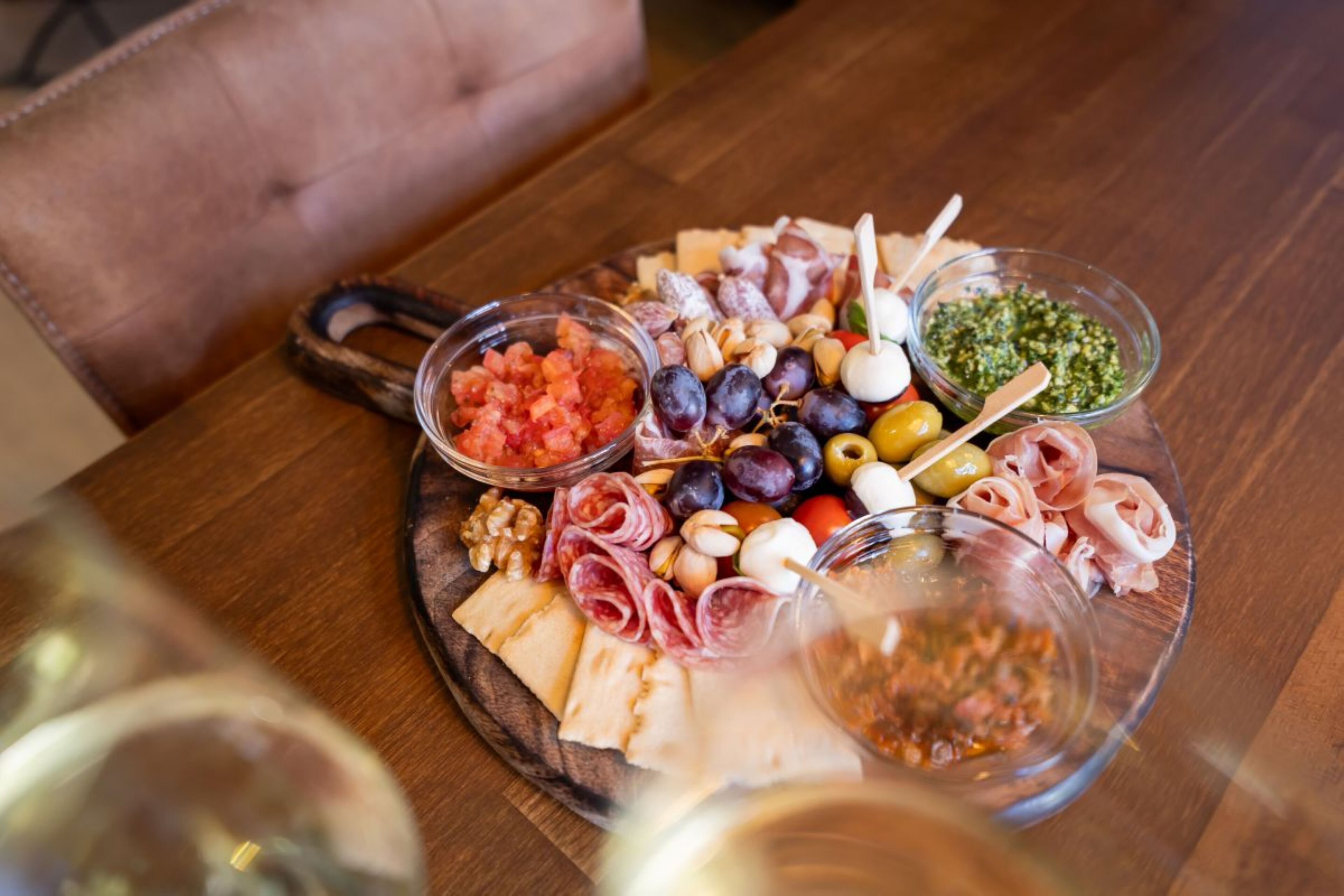 Een houten tafel met een charcuterieplank vol vleessoorten, kazen, olijven en augurken.