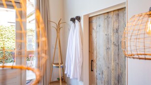 Une pièce avec une porte en bois, une serviette blanche accrochée à un crochet, un porte-manteau en bois et un luminaire suspendu.