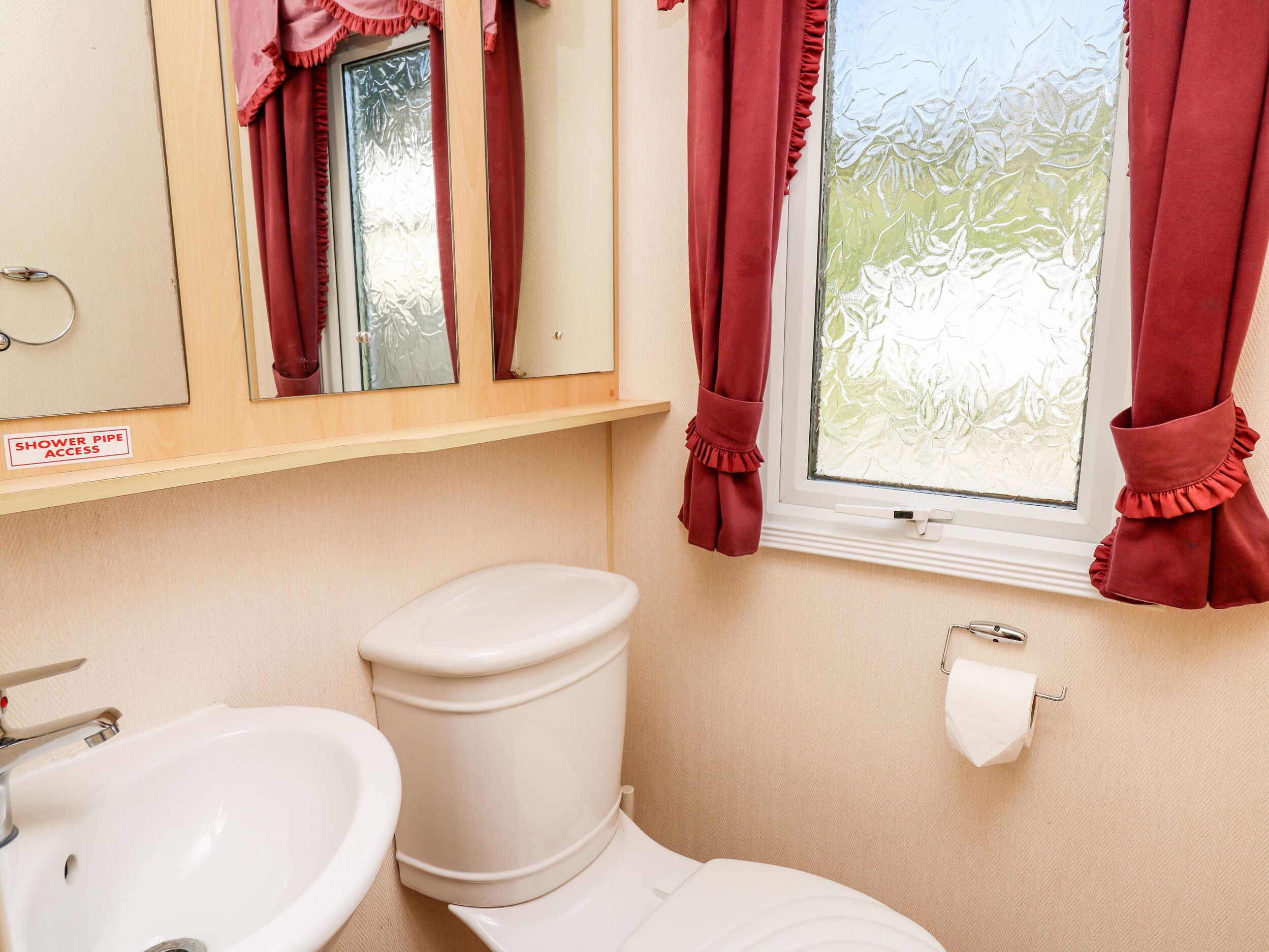 A bathroom with a toilet, sink, and a window with curtains.