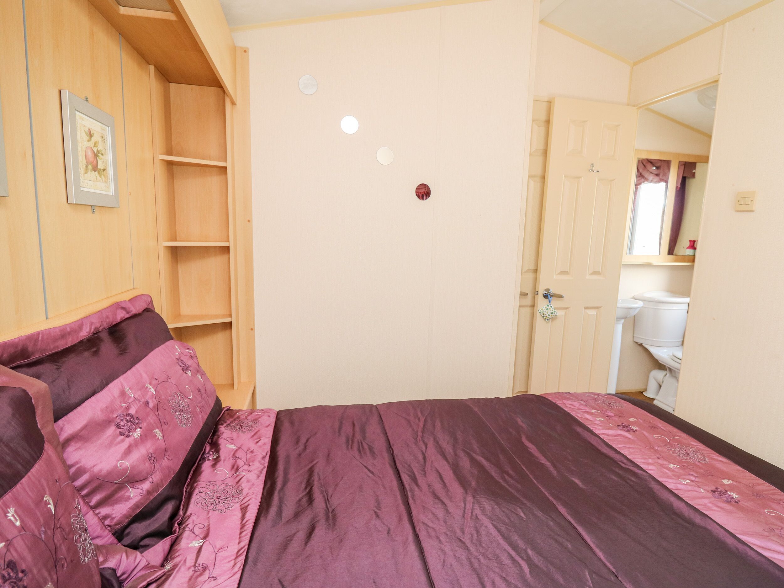 Ein Schlafzimmer mit einem Bett, einem Holzschrank, einer Tür und einem durchgehenden Türrahmen einsehbaren Badezimmer.