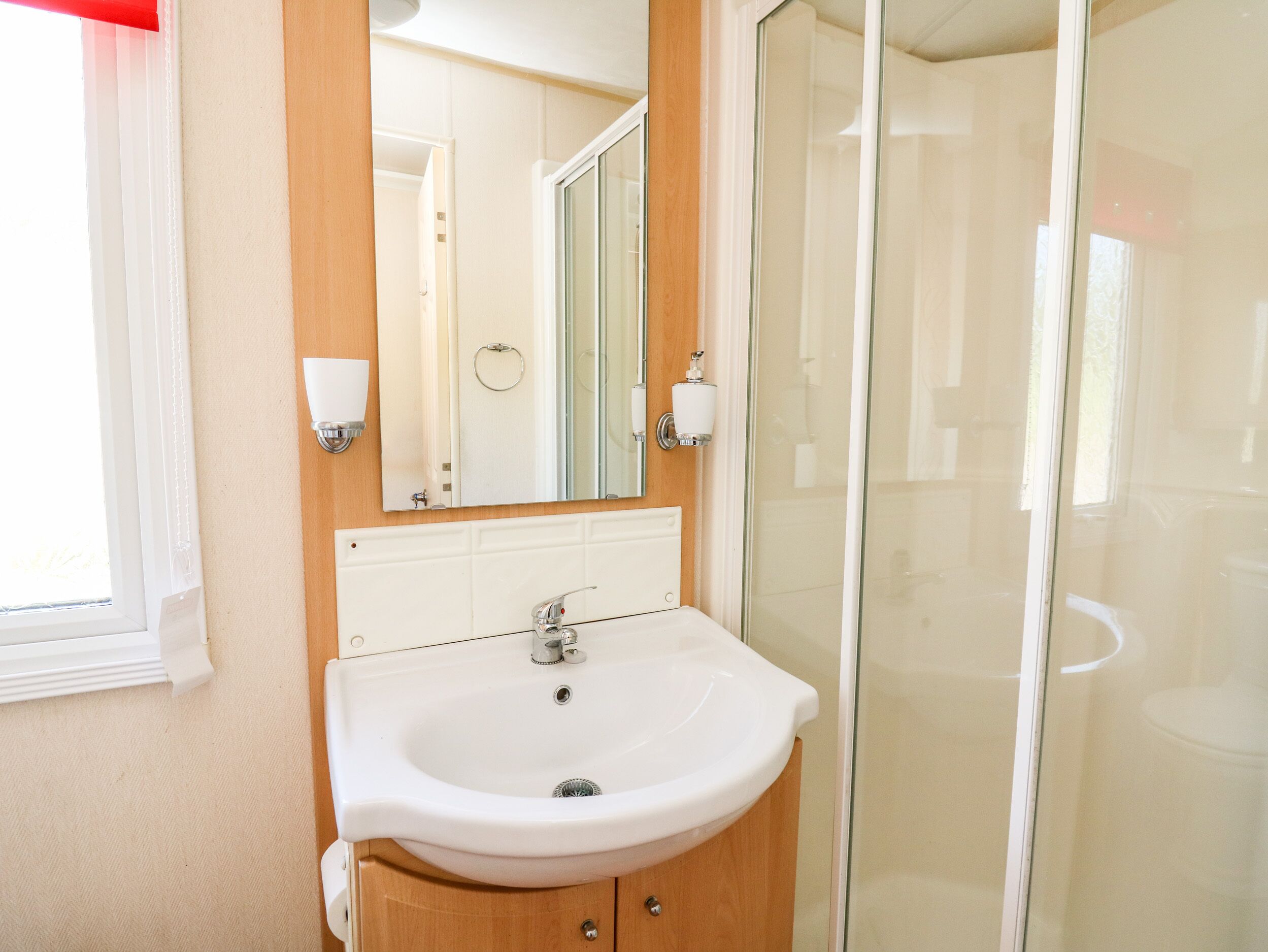 A bathroom with a white sink, wooden cabinet, and a glass shower enclosure.