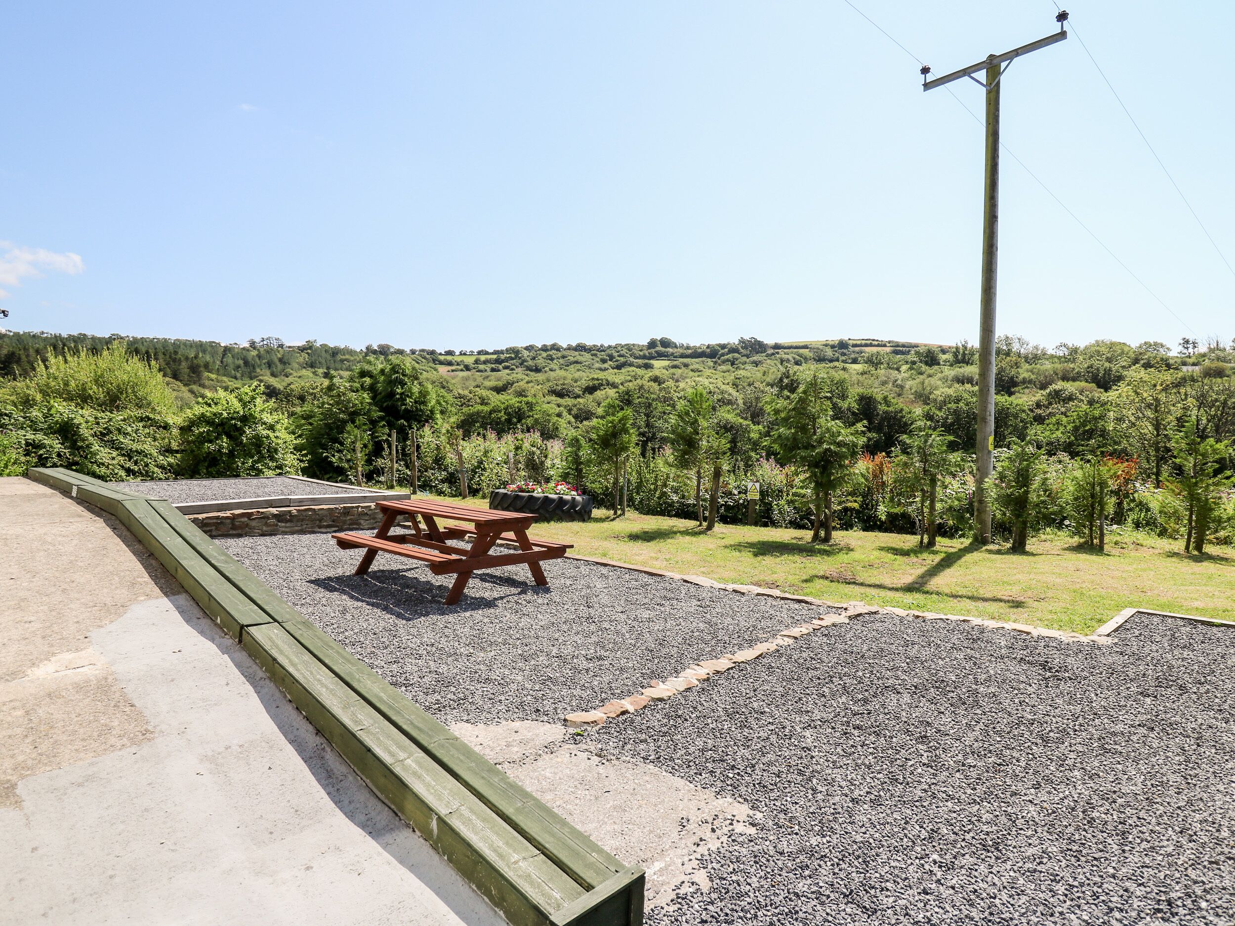 A picnic table in a park with a gravel path and a view of a forested hill.