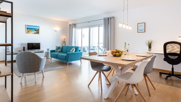 A modern living room with a blue sofa, a dining table with chairs, a TV, and a large window with curtains. - Lagos Workation Apartment (Lagos)