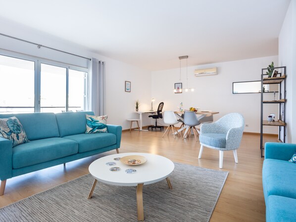 A modern living room with a blue sofa, a round coffee table, and a dining area with a white table and chairs. - Lagos Workation Apartment (Lagos)