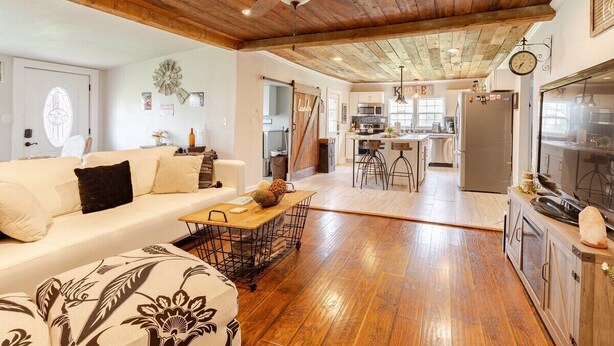 A spacious living area with a wooden ceiling, a sofa, a coffee table, and a kitchen in the background.