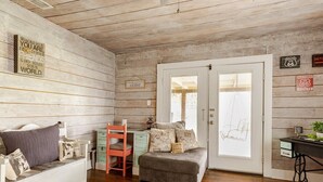 A cozy room with a wooden wall, a white door, a small desk, a bench, and a cushioned seating area.