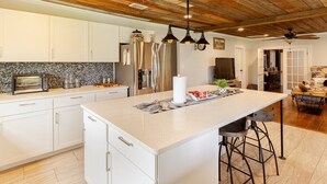 A modern kitchen with white cabinets, a large island, stainless steel appliances, and a wooden ceiling.