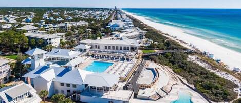 An aerial view of a coastal resort with multiple buildings, a large swimming pool, and a beach.