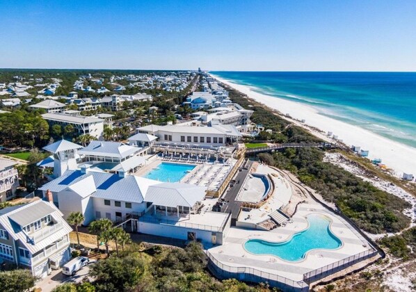 An aerial view of a coastal resort with multiple buildings, a large swimming pool, and a beach.