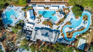 Ovenudblik over et resort med flere swimmingpools, en stor bygning og grøn vegetation omkring.