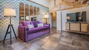 A room with a purple sofa, two floor lamps, a television, and a wicker cabinet.