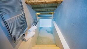 A narrow, enclosed stairwell leading to a bathtub with a wooden ceiling and a metal radiator on the left.