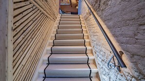 A staircase with beige carpeted steps and black metal handrails, leading to an upper level with a wooden slatted wall and a window.