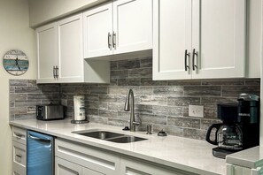 A kitchen with white cabinets, a stainless steel sink, a toaster, a kettle, and a Keurig coffee maker.