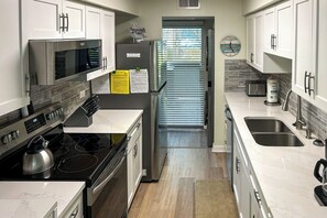 A modern kitchen with stainless steel appliances, white cabinetry, and a built-in oven. - Sunset Rentals | Treetops 4301 | Dog Friendly (Hilton Head Island)