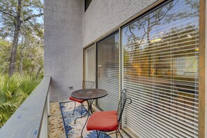 Ein Balkon mit Tisch und Stühlen, ein Fenster mit Jalousien und Blick auf Bäume und ein Gebäude.