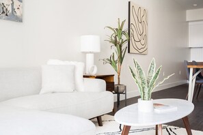 Ein modernes Wohnzimmer mit einem weißen Sofa, einem runden Couchtisch und zwei Kübelpflanzen.
