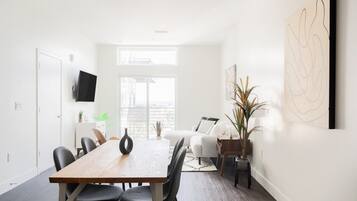 A modern living room with a dining area, a flat-screen TV mounted on the wall, and a large abstract painting.