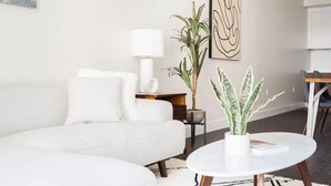 Una sala de estar moderna con un sofá blanco, una mesa redonda de centro y dos plantas en macetas.