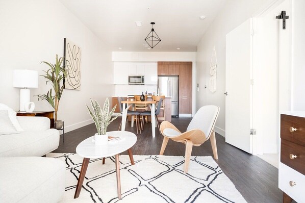 Una sala moderna con un sofá blanco, una mesa redonda y un comedor con mesa y sillas de madera.