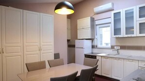 Ett kompakt kök med vita skåp, ett matbord med stolar och en hängande lampa.