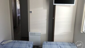 Ein kleines Zimmer mit zwei Betten, einem an der Wand montierten Flachbildfernseher und einer Heizung.