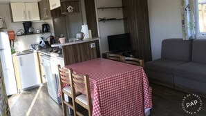 Ein kompakter Wohnbereich mit Küchenzeile, einem Essbereich mit kariertem Tisch, einer Couch und einem Fernseher.