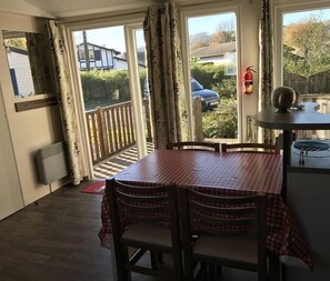 Un comedor con una mesa y sillas a cuadros, un extintor y vistas a una zona residencial a través de amplios ventanales.