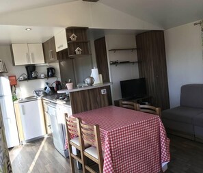Un espacio habitable compacto con kitchenette, una zona de comedor con mesa a cuadros, un sofá y una televisión.