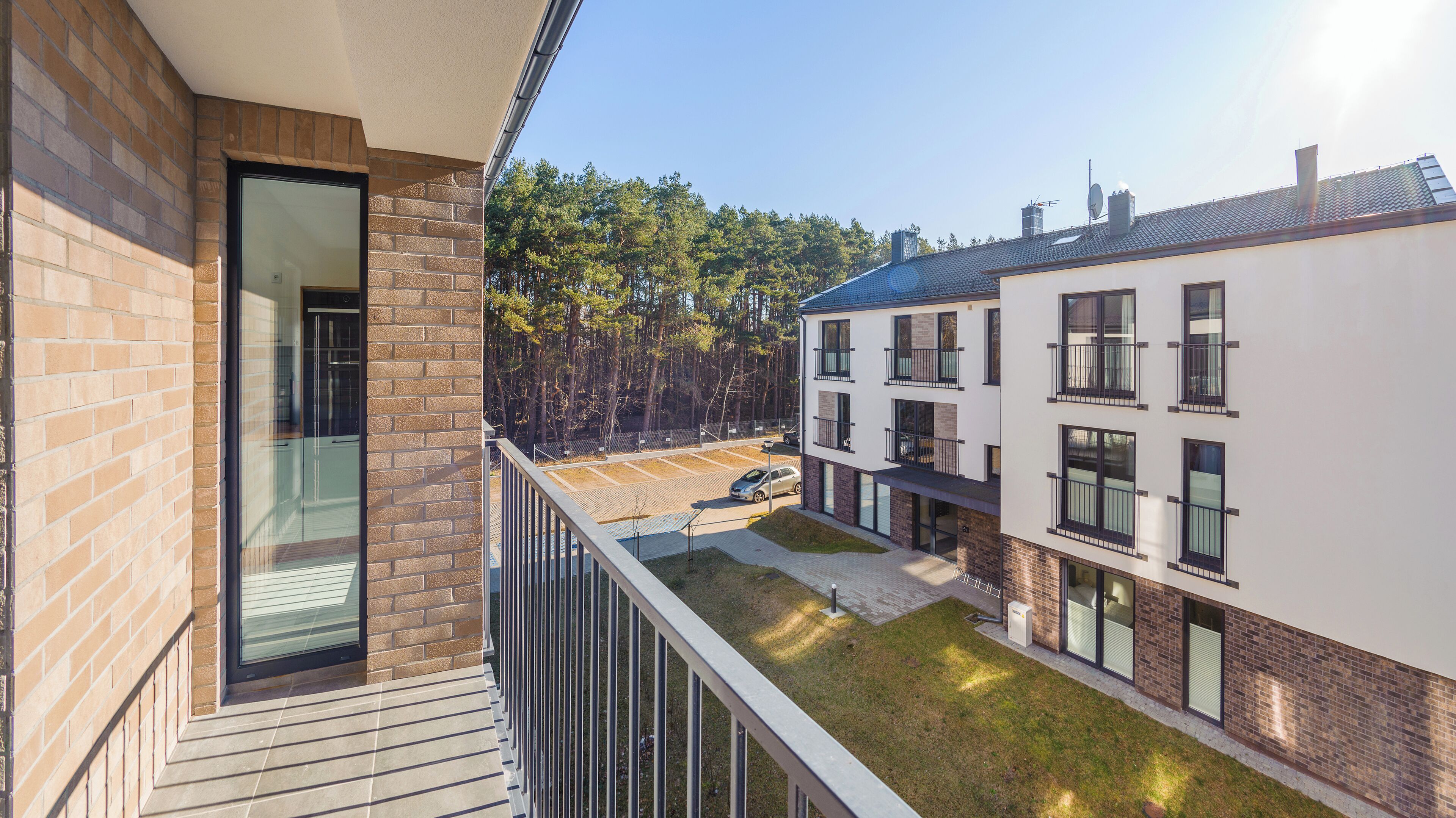 Un immeuble d’appartements moderne doté d’un balcon, d’un espace de stationnement et offrant une vue sur une forêt.