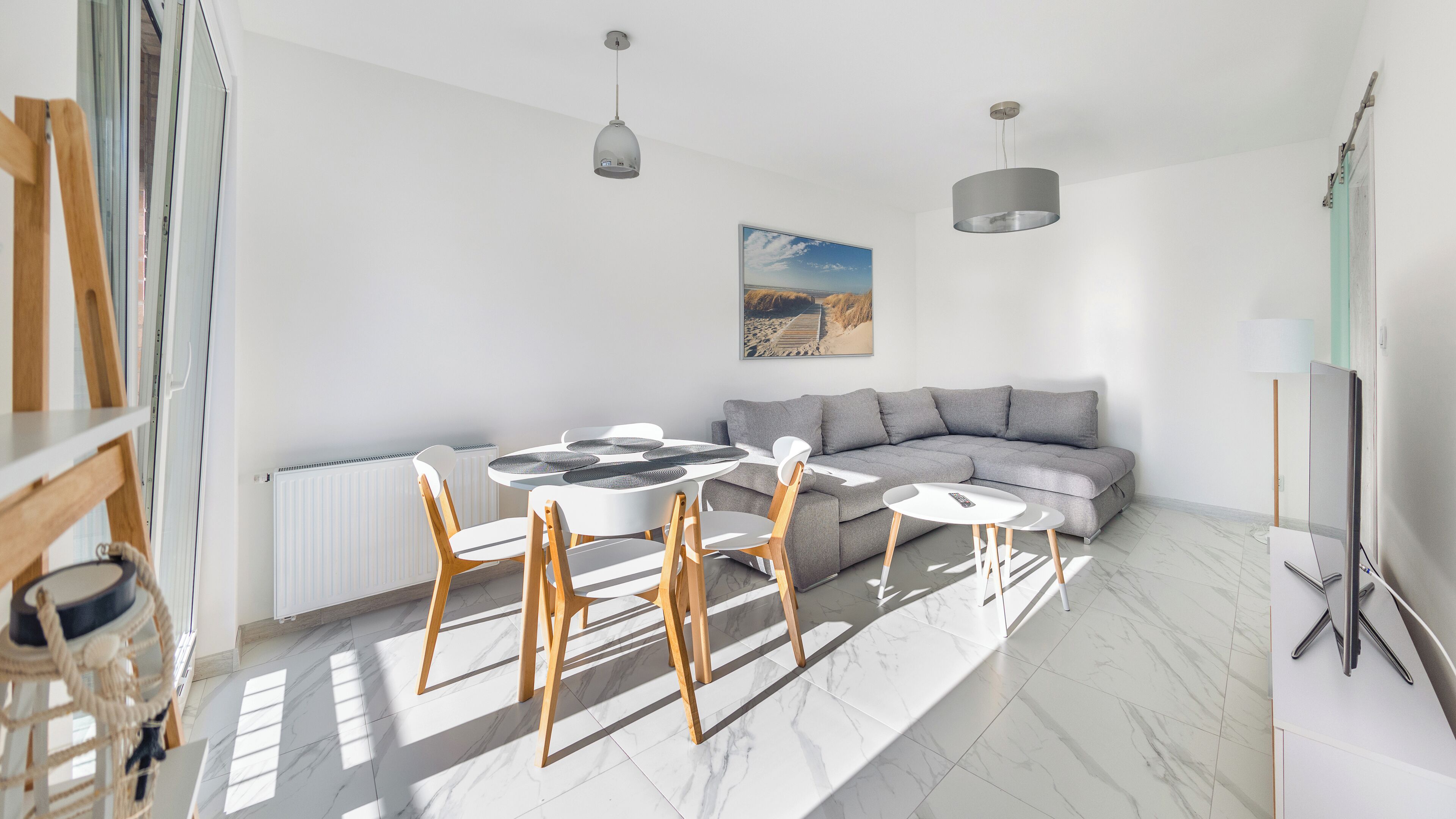 A modern living room with a sectional sofa, a dining table with chairs, and a large window allowing natural light.