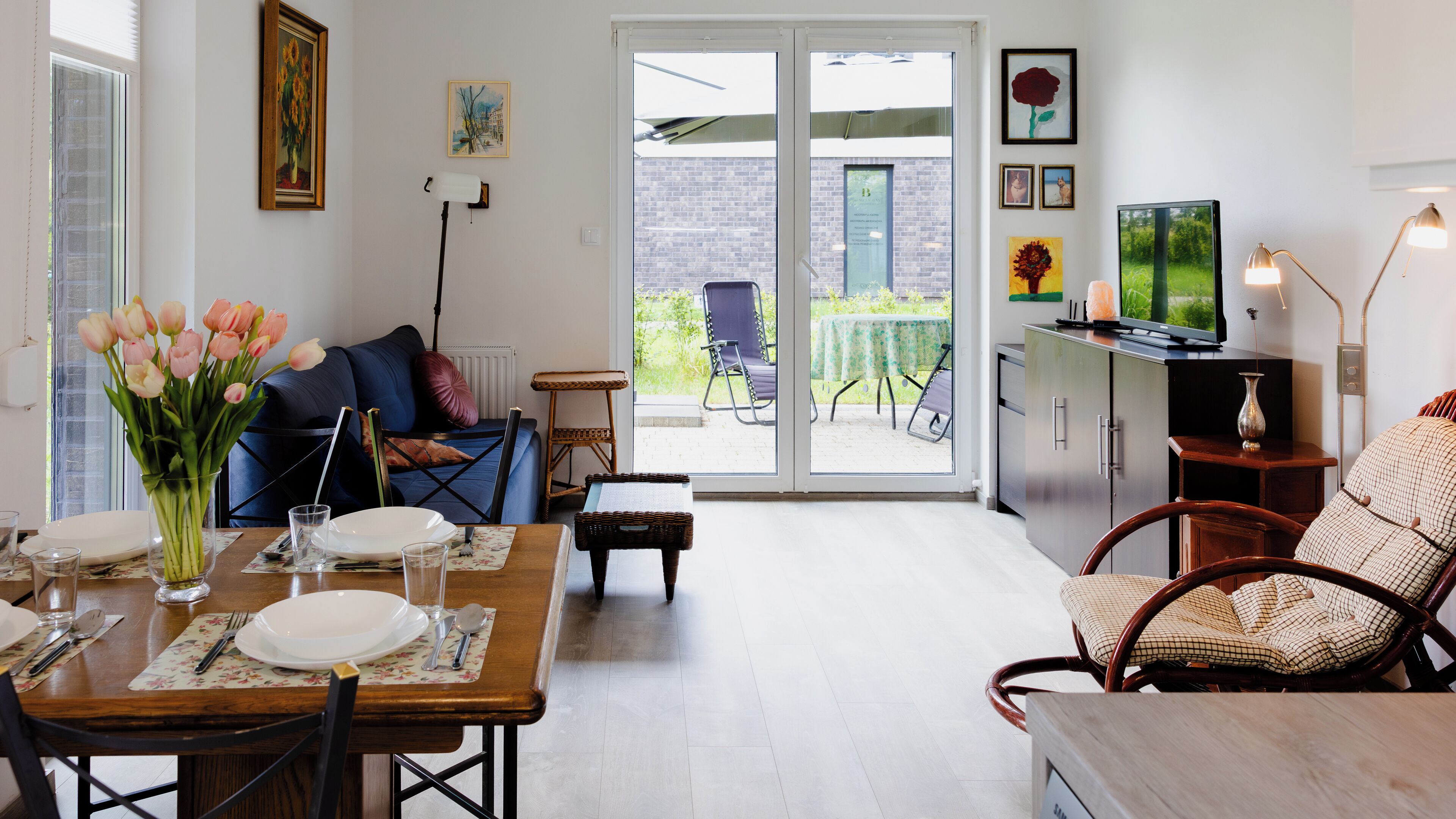 A dining area with a table set for two, a sofa, and a TV in the background.
