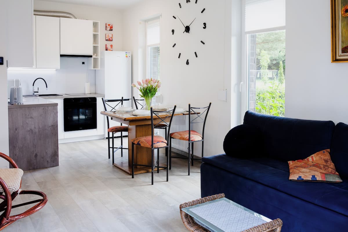 A modern living room with a dark blue sofa, a dining area with a wooden table and chairs, and a kitchen in the background.